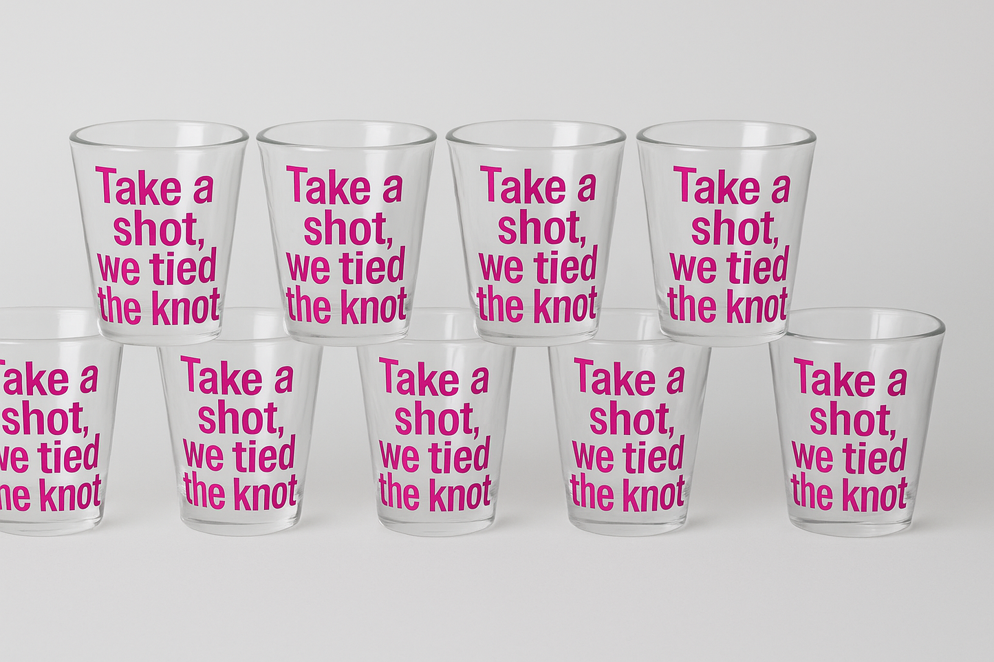 Set of clear glasses with pink text 'Take a shot, we tied the knot' on a white background