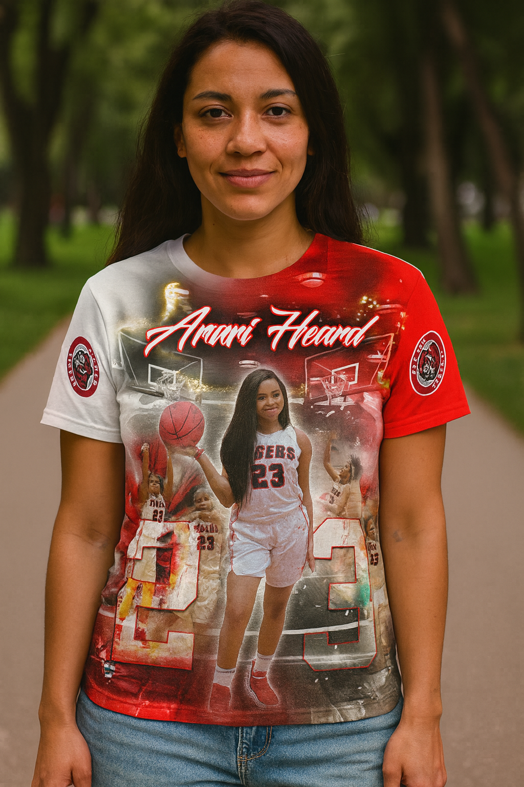 Young woman wearing a vibrant all-over print T-shirt featuring basketball player Anari Heard, with dynamic red, white, and black graphics and action shots; modeled outdoors in a park setting.