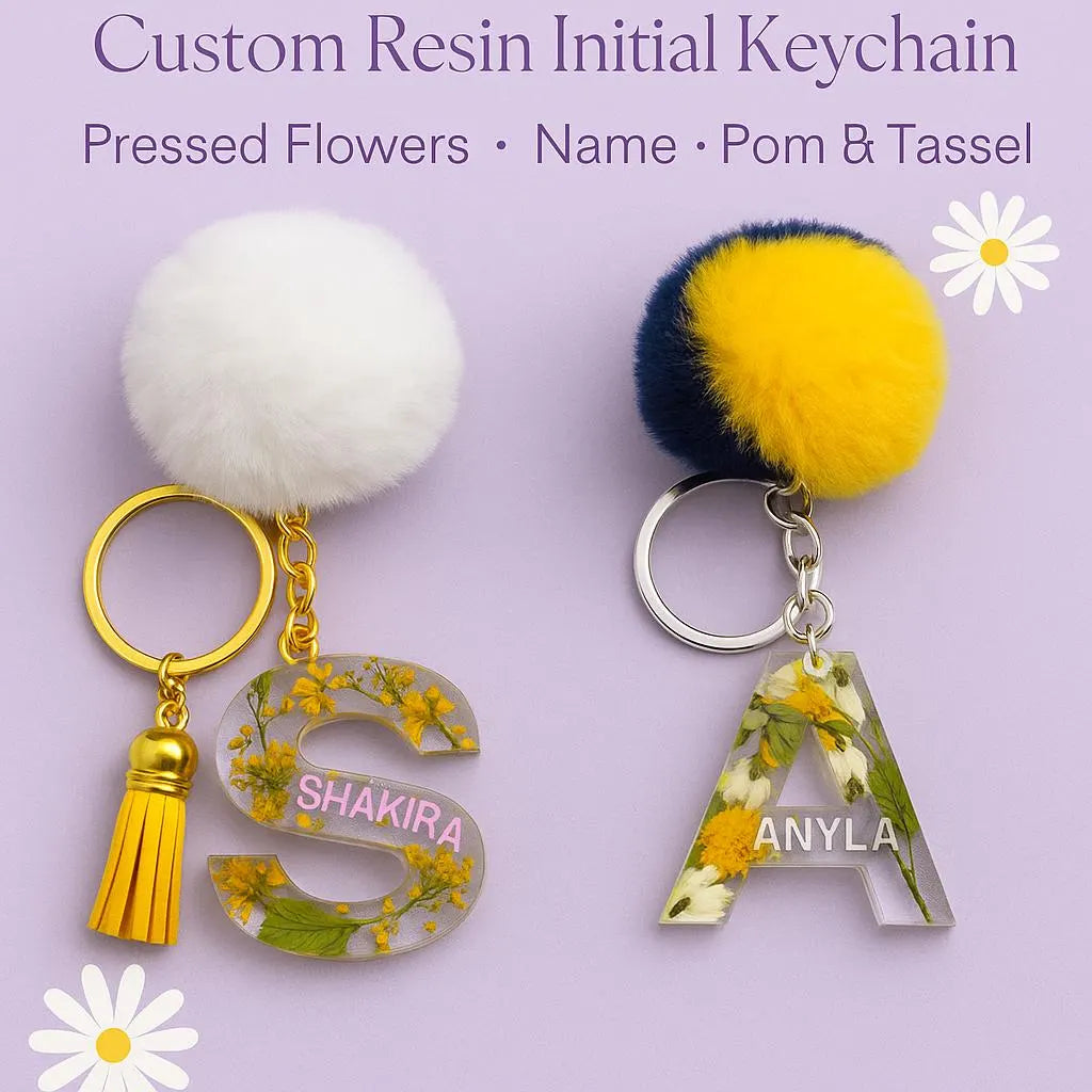 Two custom resin initial keychains with pom-poms and tassels on a light purple background.