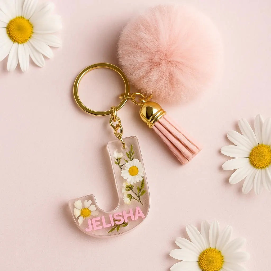 Personalized resin keychain with the letter J, embedded daisies, pink name label Jelisha, gold key ring, pink tassel, and pompom charm