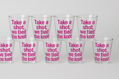 Set of clear glasses with pink text 'Take a shot, we tied the knot' on a white background