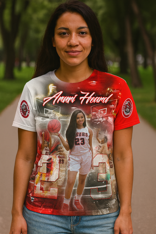 Young woman wearing a vibrant all-over print T-shirt featuring basketball player Anari Heard, with dynamic red, white, and black graphics and action shots; modeled outdoors in a park setting.